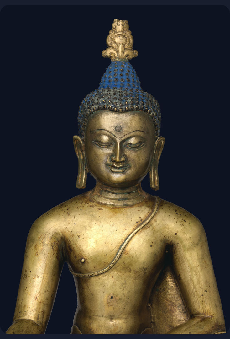 Golden statue of a buddha with long drooping earlobes and a blue cranial bump looking downwards